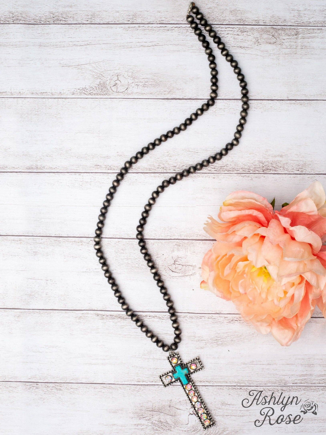Necklace with cross pendant on a wooden surface with a flower